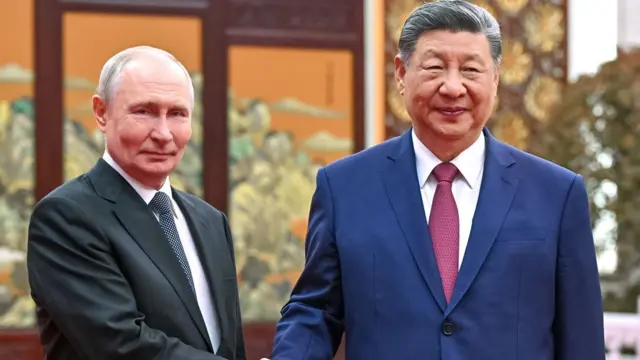 普京（左）与习近平（右）在北京人民大会堂茶叙时握手供媒体记者拍摄；普京身穿深色西装、白色衬衣，结波尔卡圆点领带；习近平身穿海军蓝色西装、白色衬衣，结红色领带（20/5/2026）